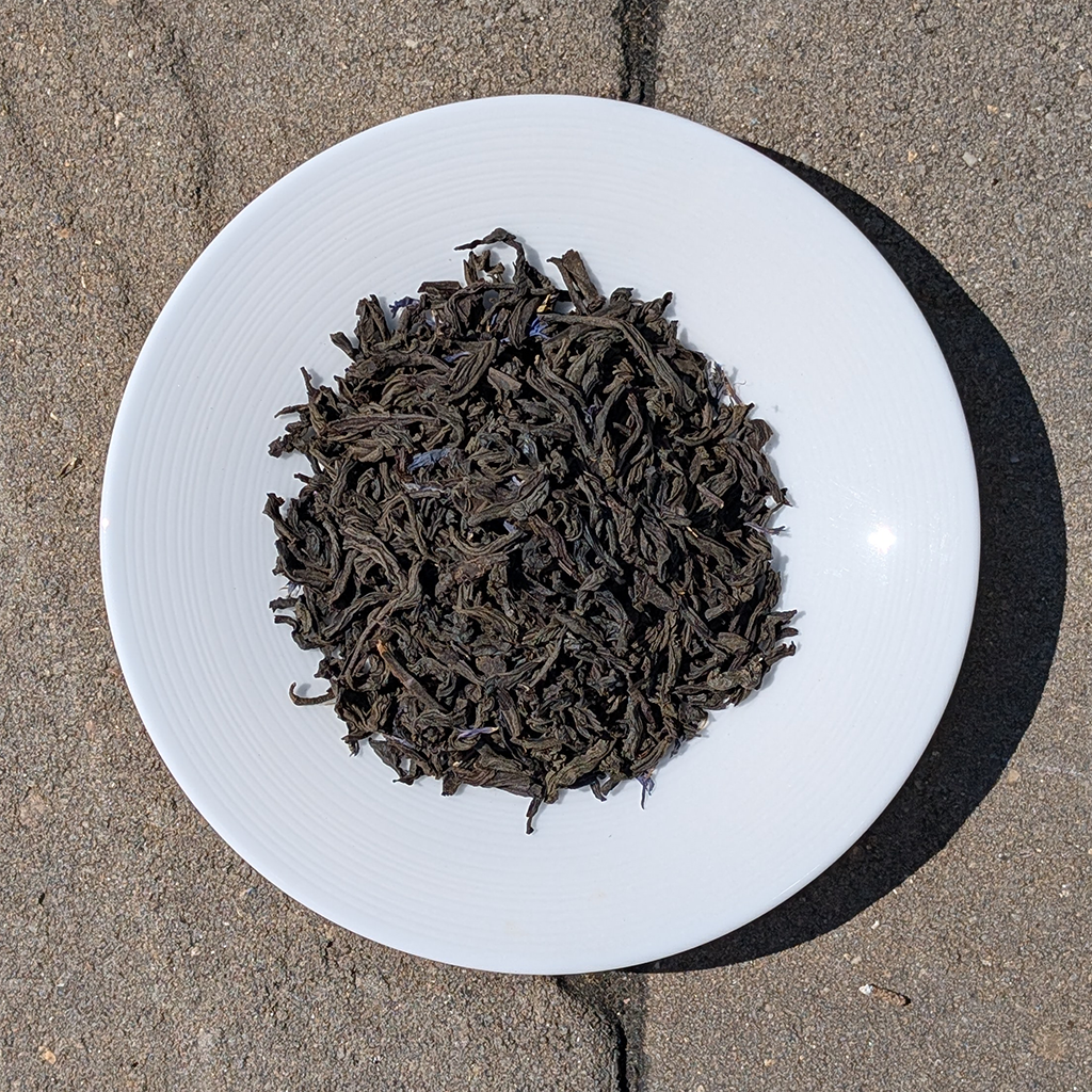 Dry black tea leaves on a white plate with a concrete floor background