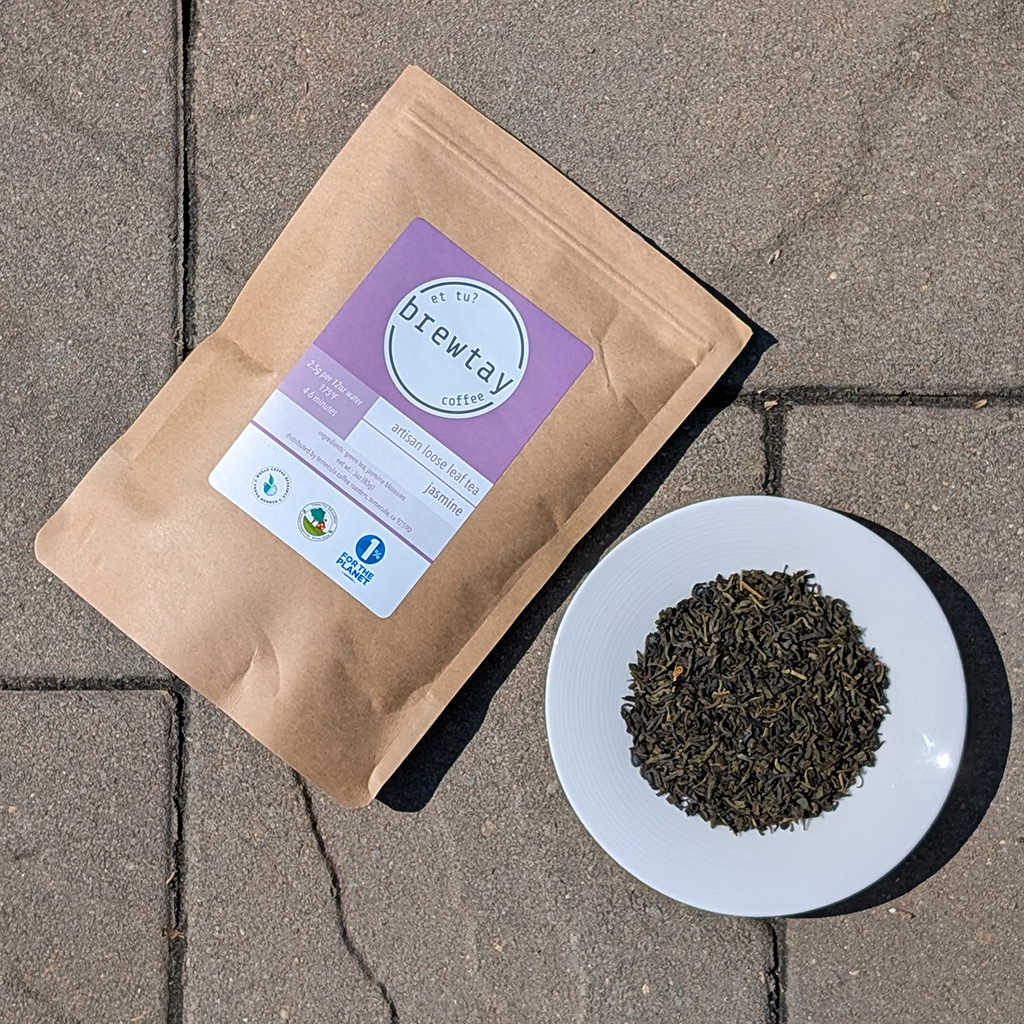 Kraft paper tea bag with a purple label on a stone surface, next to a white plate with tea leaves.