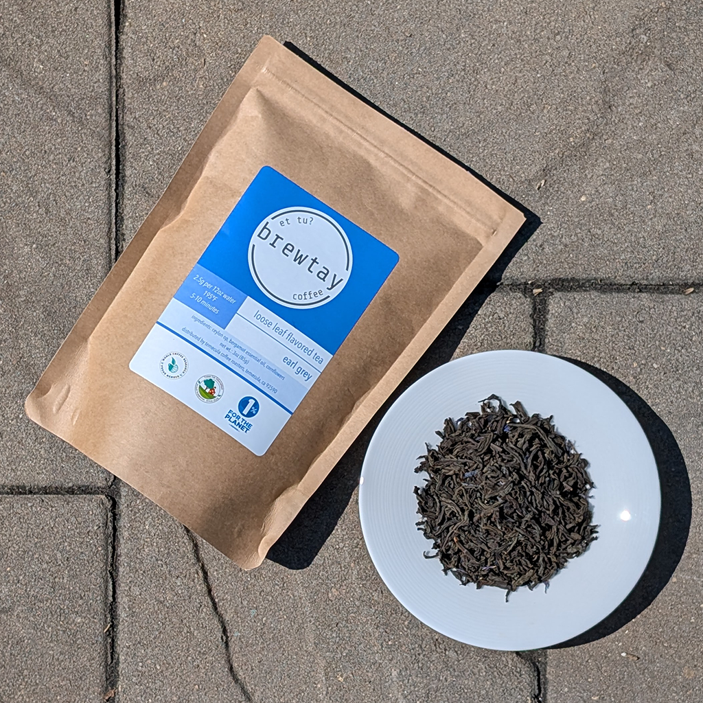 Brown tea packaging with blue label on a concrete surface, accompanied by a white plate with loose tea leaves.
