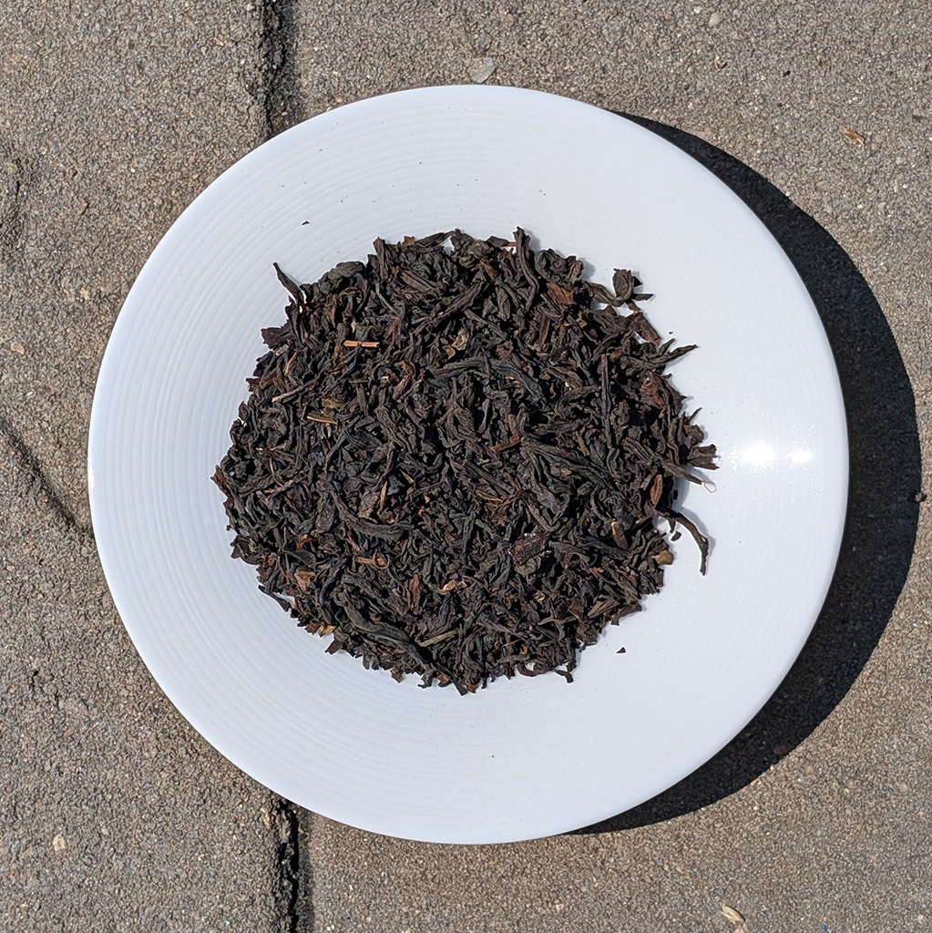Dry black tea leaves on a white plate with a concrete floor background